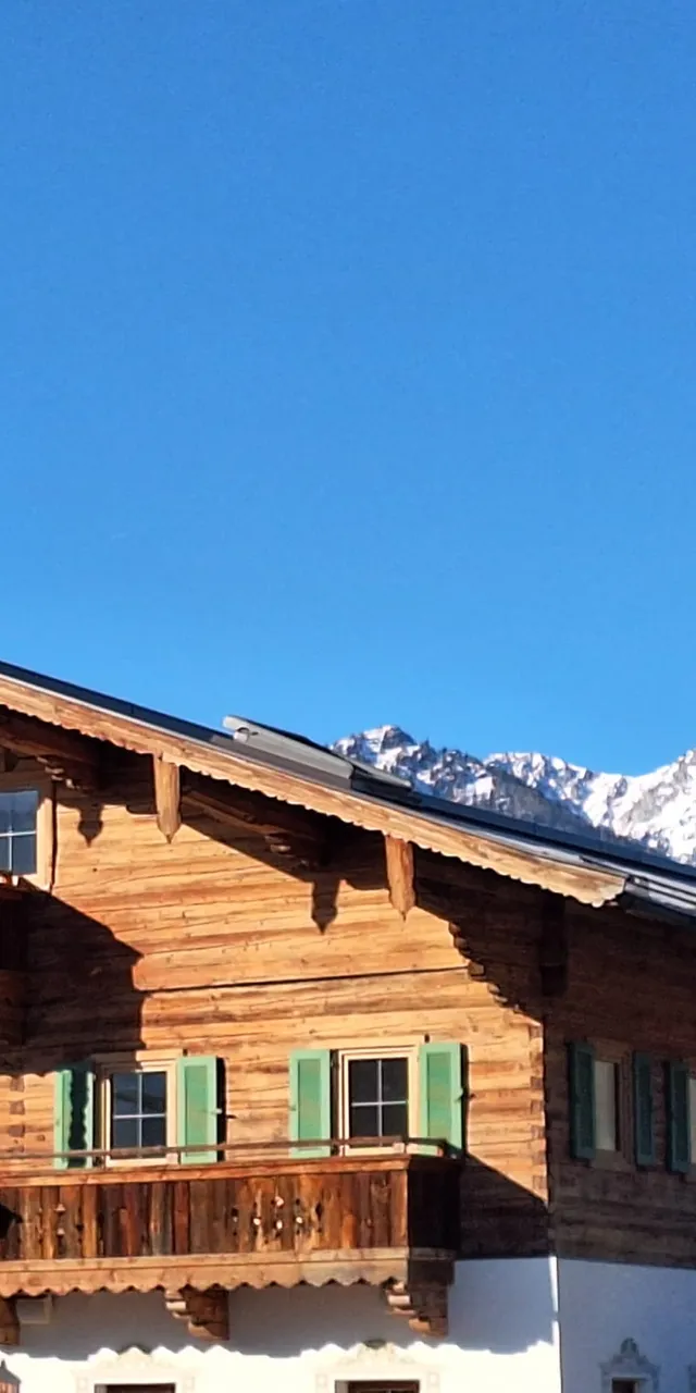 Holzchalet in den Alpen mit Bergen im Hintergrund unter klarem Himmel