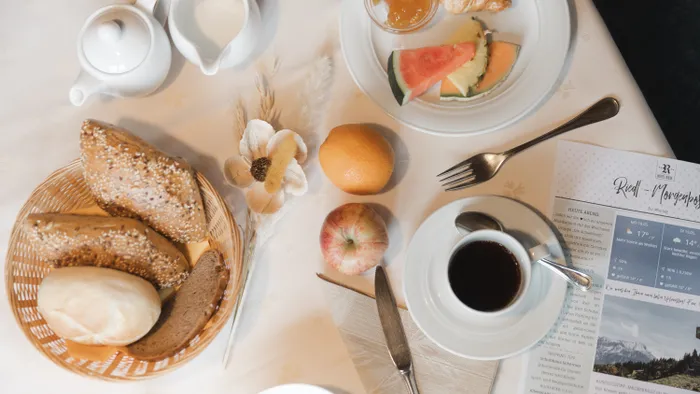 Frühstückstisch mit Brotkorb, Kaffee, Obst und einem Nachrichtenblatt