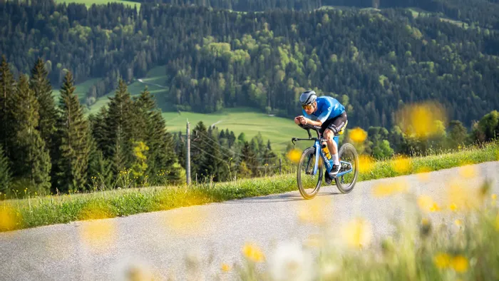 Cyclist in aerodynamic position riding on mountain road through scenic forest landscape