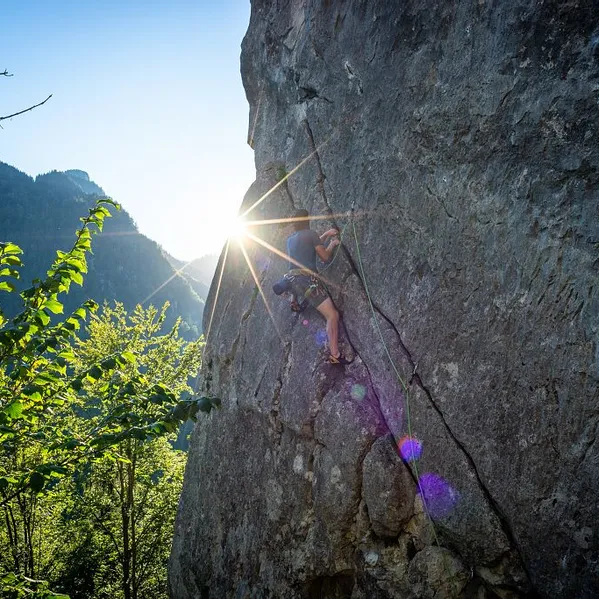 Rock climber scaling a steep cliff face with sunlight shining through mountain forest