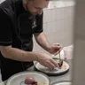 Chef plating gourmet dessert with berry garnish in professional kitchen