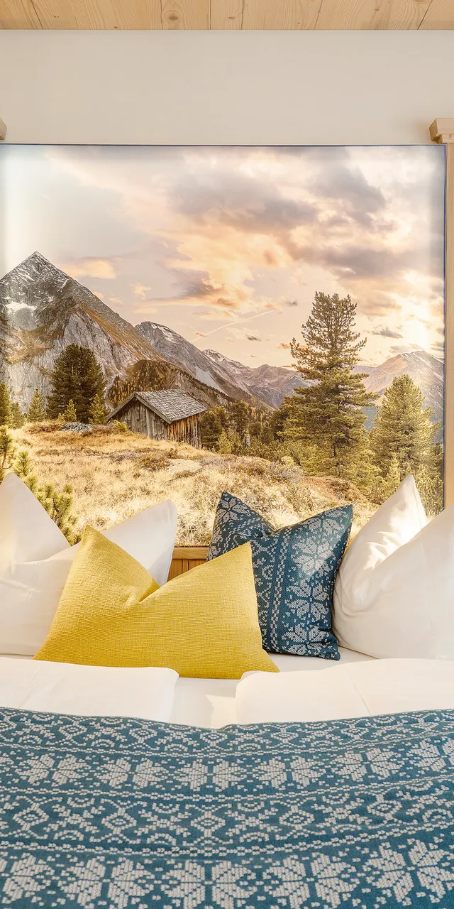 Gemütliches Alpenhotelzimmer mit Holzeinrichtung, gemustertem Bettbezug und Berglandschaftsbild