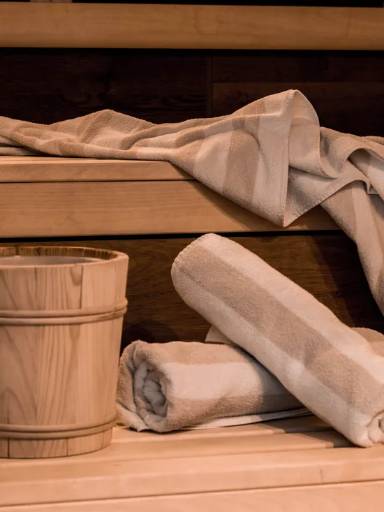 Sauna-Innenraum mit gerollten Handtüchern, Holzeimer und Kelle auf hellen Holzbänken
