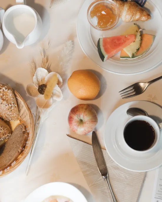 Frühstückstisch mit Brotkorb, Kaffee, Obst und einem Nachrichtenblatt