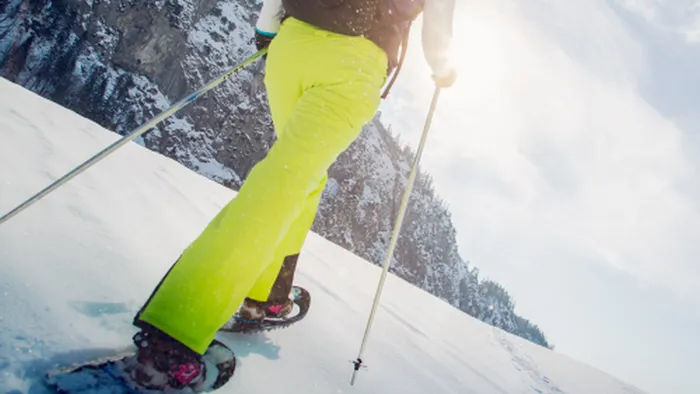 Person snowshoeing uphill in bright yellow pants on a sunny winter day in the mountains