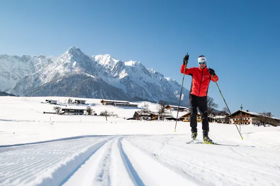 Langläufer in roter Jacke auf Loipenspur im verschneiten Alpendorf