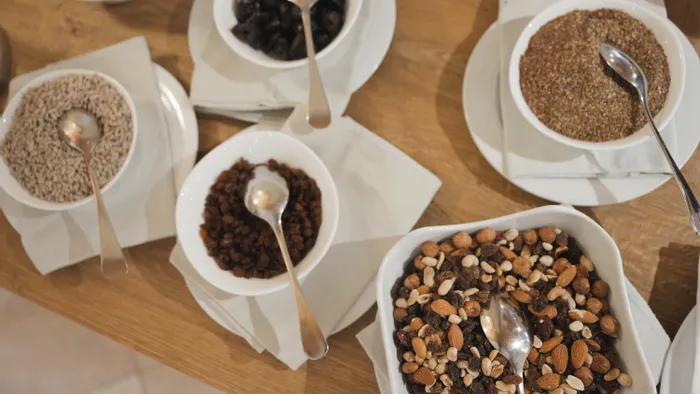 Auswahl an Trockenfrüchten, Samen und Nüssen in Schalen mit Löffeln auf Holztisch