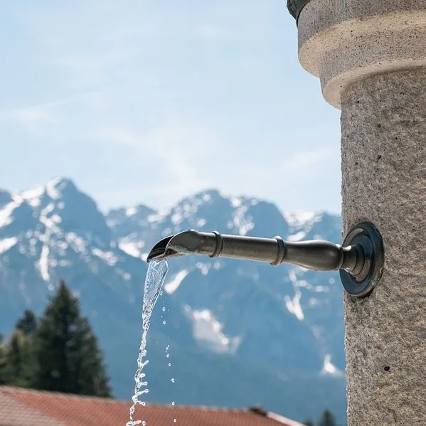 Bergbrunnen mit fließendem Wasser vor Alpenkulisse