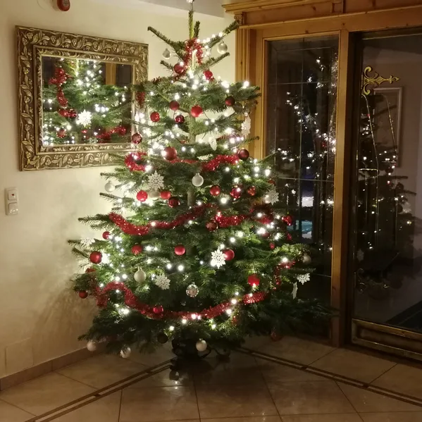 Geschmückter Weihnachtsbaum mit roten und weißen Kugeln und Lichtern in einem gemütlichen Wohnzimmer
