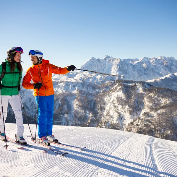 Paar in bunter Skibekleidung genießt sonnigen Tag auf schneebedecktem Alpengipfel