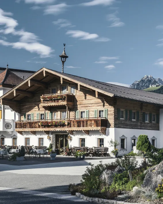 Traditionelles Alpenhotel mit blumengeschmückten Balkonen in Bergdorfkulisse