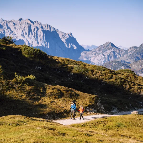Zwei Wanderer auf einem Bergweg mit Alpenpanorama im Hintergrund