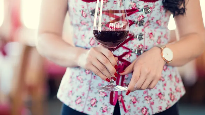Frau im Blumen-Dirndl hält ein Glas Rotwein auf traditionellem Fest