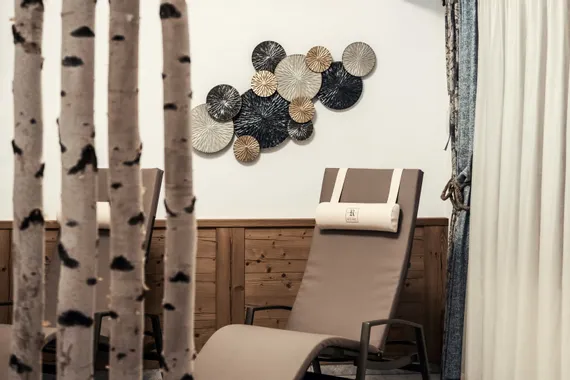 Ruhelounge mit beigen Liegestühlen, Birkenstämmen und dekorativer Wandkunst