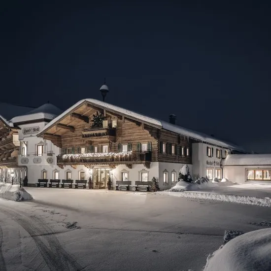 Gemütliches Alpenhotel im Winter, nachts warm beleuchtet mit schneebedecktem Dach und Umgebung