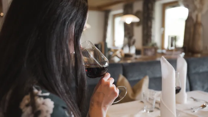 Woman sipping red wine at a restaurant table with white napkins