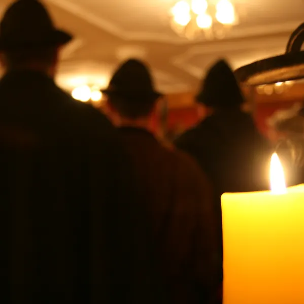 Brennende gelbe Kerze im Fokus mit unscharfen Personen mit Hüten bei Veranstaltung