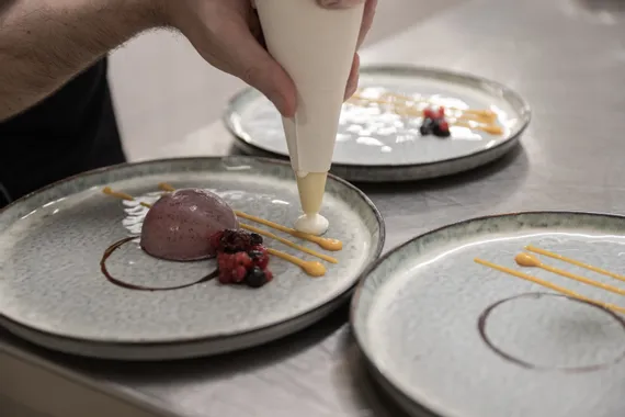 Chef decorating gourmet dessert with fruit mousse, sauce, and fresh berries on ceramic plate