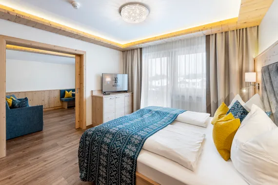 Modernes Hotelzimmer mit Doppelbett, Fernseher, Holzelementen und angrenzendem Loungebereich