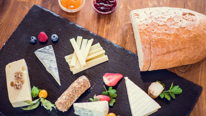 Assorted gourmet cheeses with berries, bread, and fruit preserves on a slate serving board