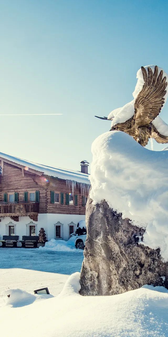 Schneebedecktes Alpenhotel mit Adlerstatue an einem sonnigen Wintertag in Bayern