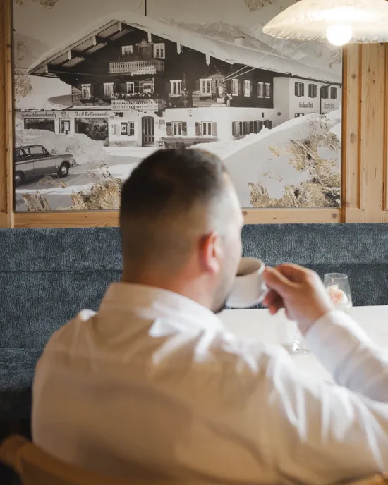 Mann im weißen Hemd trinkt Kaffee, betrachtet großes Vintage-Foto eines Chalet-Interieurs
