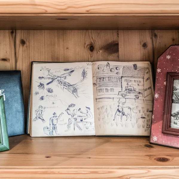 Wooden shelf with photo frames, guestbook, and hand-drawn sketches of an alpine guesthouse