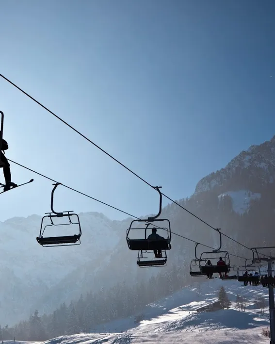 Skiers riding a chairlift over a snowy mountain slope under clear blue sky