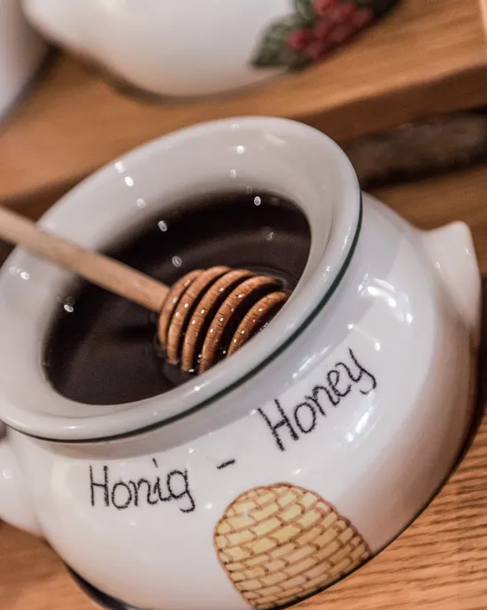 Ceramic honey jar with dipper filled with dark honey on wooden tray