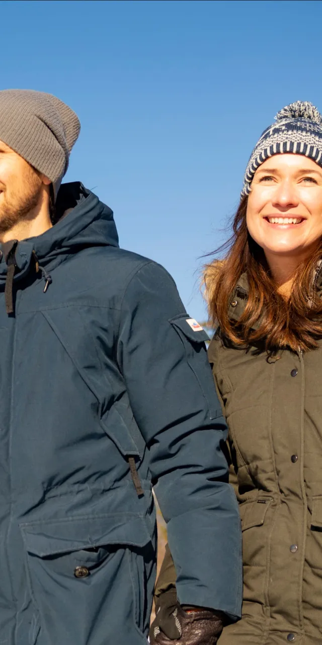 Smiling couple in winter jackets walking outdoors on a sunny snowy day