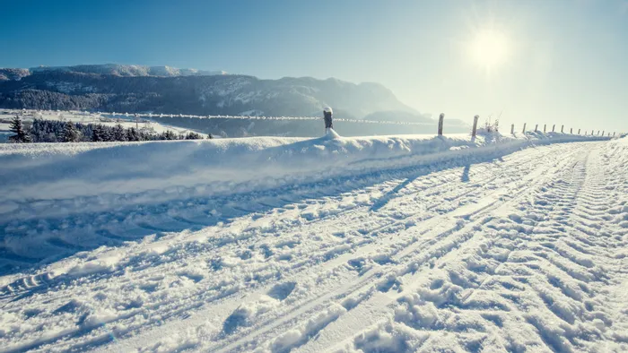 Snow-covered mountain road with tire tracks under bright winter sun