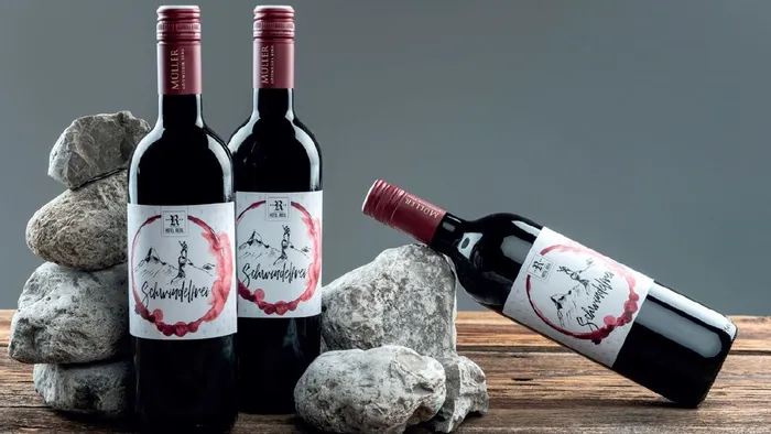 Red wine bottles labeled Schwindelfrei from Hotel Bergl arranged with rocks on wooden surface