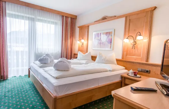Gemütliches Hotelzimmer mit Doppelbett, Holzmöbeln und Bergblick durch großes Fenster