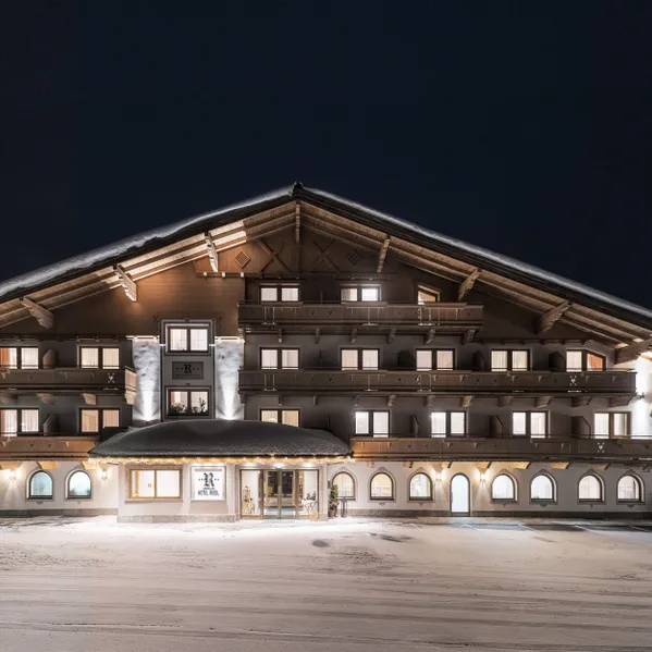 Alpenhotel mit Holzbalkonen und warmem Licht in verschneiter Winternacht