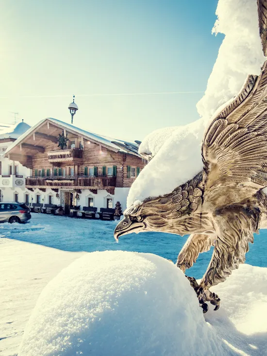 Schneebedeckte Bronzestadue eines Adlers vor einem Alpenhotel in Winterlandschaft