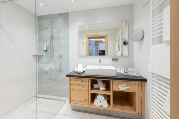 Modernes Hotelbad mit begehbarer Dusche, Holzwaschtisch und gerollten weißen Handtüchern