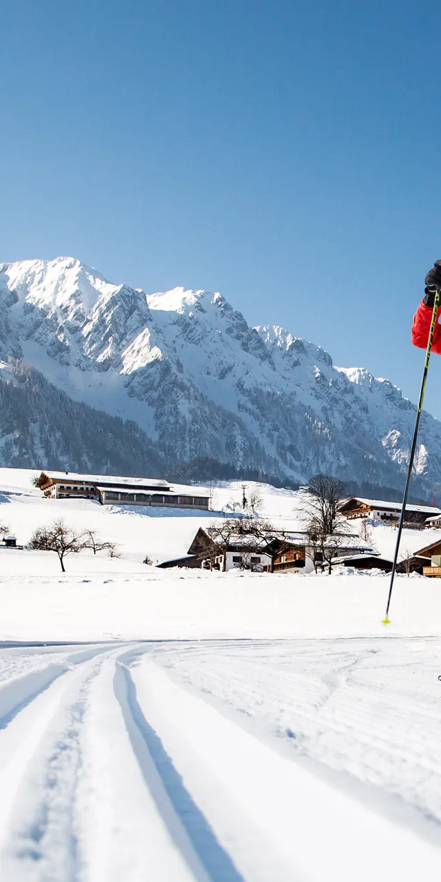 Cross-country skier in red jacket gliding on snow trail in Alpine mountain village