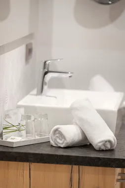 Rolled white towels and toiletries beside a modern bathroom sink