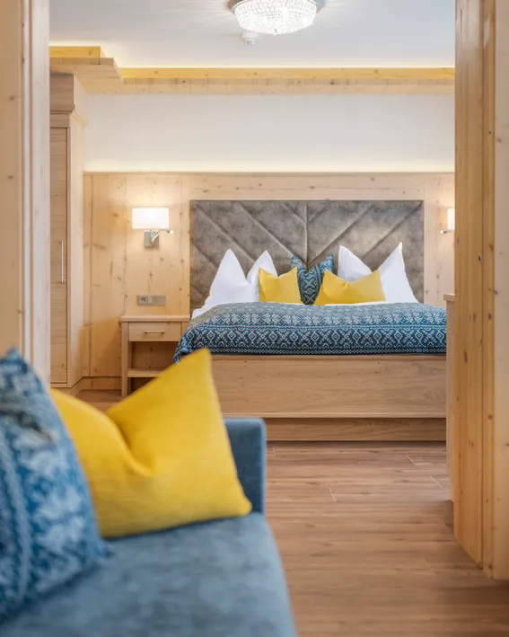 Gemütliches Hotelzimmer mit Holzmöbeln, Doppelbett und blau-gelben Zierkissen