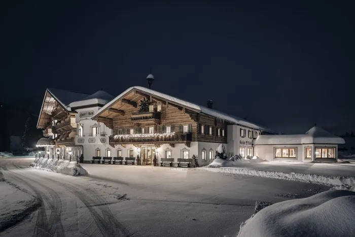 Cozy alpine hotel in winter, warmly lit at night with snow-covered roof and surroundings