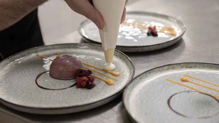 Koch verziert Gourmet-Dessertteller mit Mousse, Beerenkompott und Soßentropfen