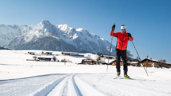 Langläufer in roter Jacke auf Loipenspur im verschneiten Alpendorf