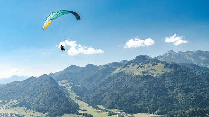 Gleitschirmflieger über Alpenbergen bei klarem Sonnenschein nahe einem kleinen Dorf