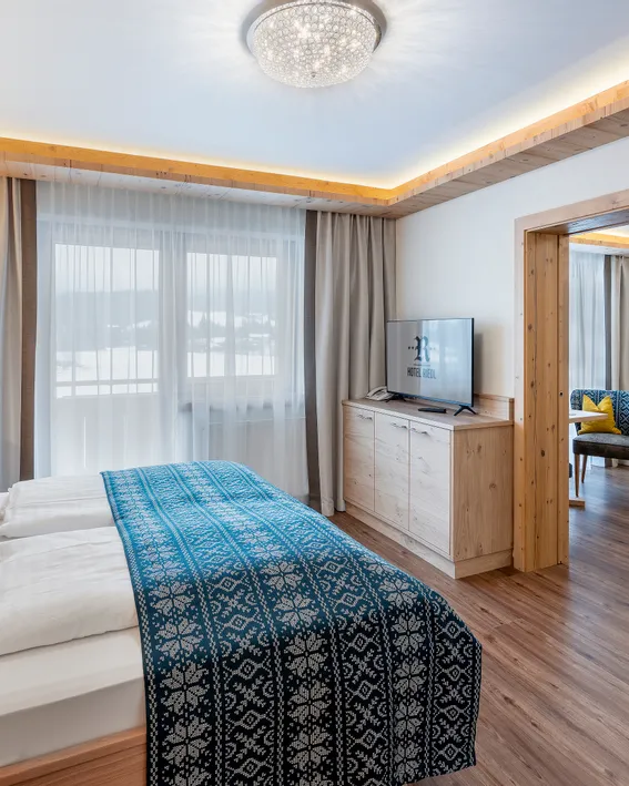 Modern hotel suite with double bed, wooden furnishings, TV, and mountain view