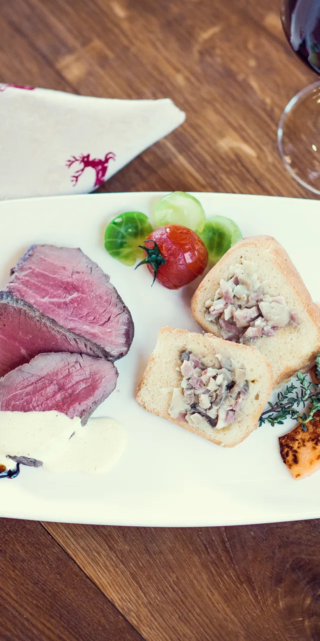 Gourmet-Rindfleischscheiben mit Sahnesoße, gefülltem Brot, Trauben und Rotwein auf Holztisch