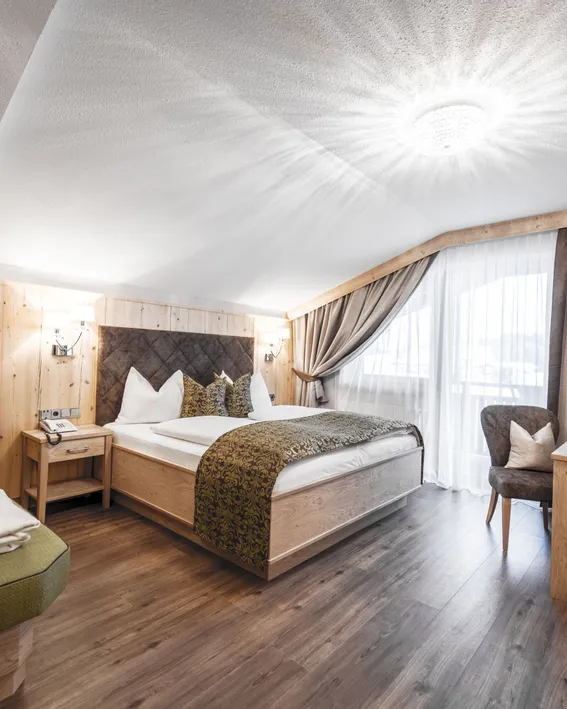 Gemütliches Alpenhotelzimmer mit Holzeinrichtung, Doppelbett, Kamin und Tageslicht