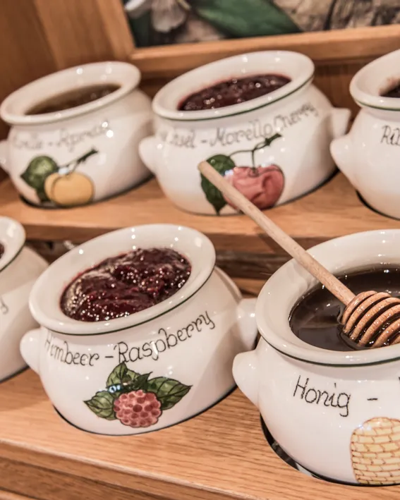 Ceramic jars with assorted fruit jams and honey on wooden display shelf