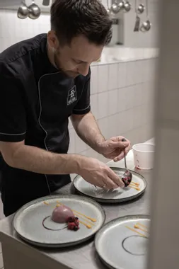 Koch richtet Gourmetdessert mit Beerenkompott und Sauce in Profiküche an