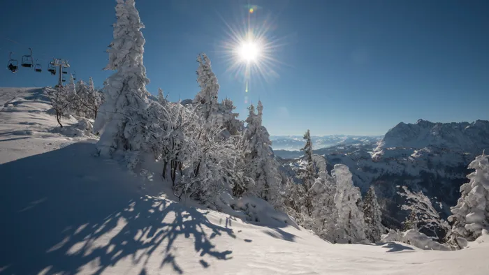 Sonnige Winterlandschaft mit schneebedeckten Bäumen und Skiliften in den Alpen