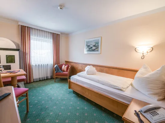 Gemütliches Hotel-Einzelzimmer mit Holzmöbeln, grünem Teppich und Schreibtisch bei Tageslicht